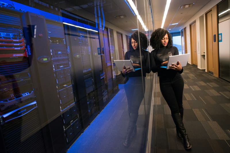 A woman checking a tablet beside a server room — licensed illustration, not a person in the BLS count. Washington.