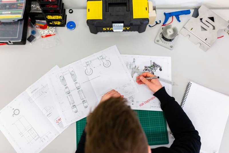 A woman measuring a part against an engineering drawing — licensed illustration, not a person in the BLS count. Illinois.