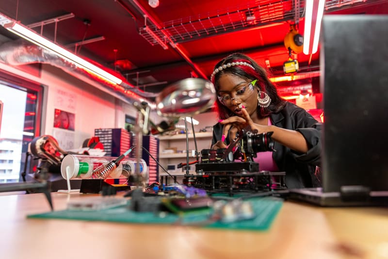A woman assembling a drone at a workbench — licensed illustration, not a person in the BLS count. Campaign hub portrait grid.