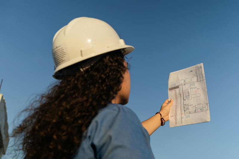 A woman reading site plans in a hard hat — licensed illustration, not a person in the BLS count. Blanco County, Texas.