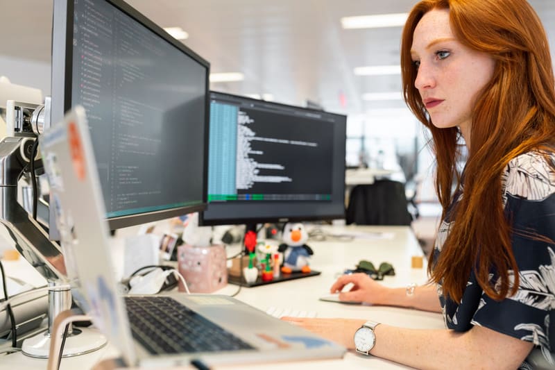 A woman working at dual monitors with code on the screen — licensed illustration, not a person in the BLS count. Nebraska.